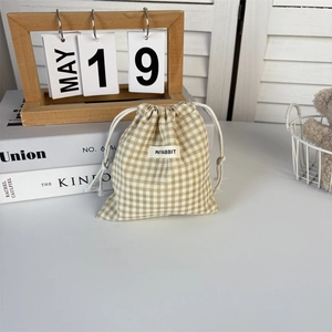 Detailed view of checkered drawstring pouch with woven logo on soft white table
