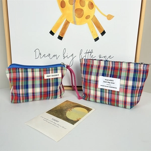Close-up of plaid fabric makeup bags with pink wrist straps and metal zipper detail