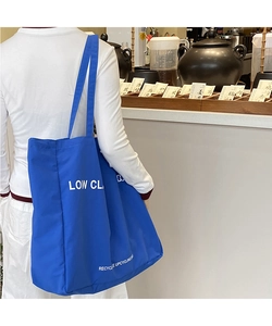 Blue canvas tote bag with white letter print shown on a model in a minimal setting
