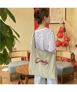 Close-up of a light green nylon tote bag featuring red Candy lettering and brown straps
