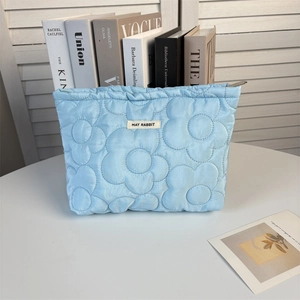 Detail of light blue quilted makeup bag featuring floral stitching and metal zipper