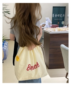 Detail of cream canvas Beach tote bag featuring red embroidery and yellow side tag