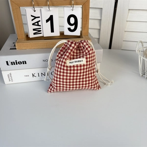 Close-up of red and white plaid drawstring pouch with logo label on stack of books