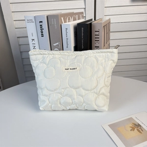 Macro shot of white floral quilted makeup bag with MAY RABBIT label on a desk