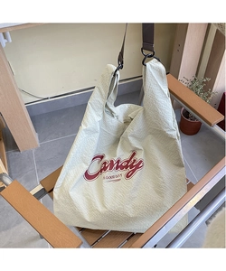 Close-up of beige plaid nylon tote bag with red Candy lettering on a wooden chair