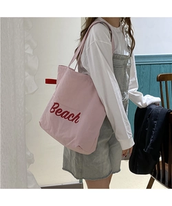Detail of pink nylon tote bag with red Beach embroidery shown on model shoulder