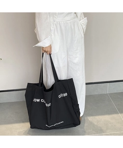 Detail of a large black canvas tote bag with white lettering on a model with white clothes