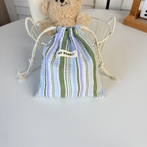 Détail de la pochette rayée bleue et violette avec étiquette May Rabbit dans un décor doux
