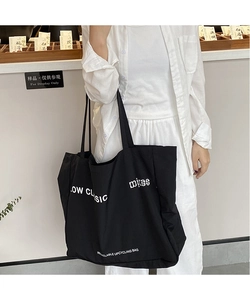 Detail of minimalist black canvas tote bag with white lettering on model shoulder