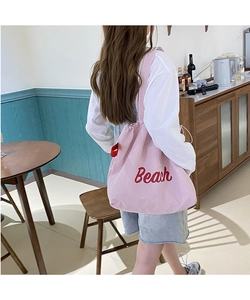 Pink nylon tote bag with red Beach letter print shown on a model in a cozy indoor setting