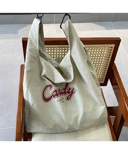 Close-up of light green seersucker tote bag with red Candy lettering on a wooden chair