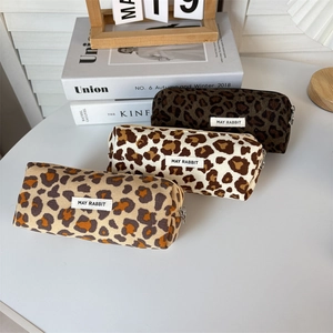 Three leopard print corduroy pencil cases in brown, cream, and tan on a white table