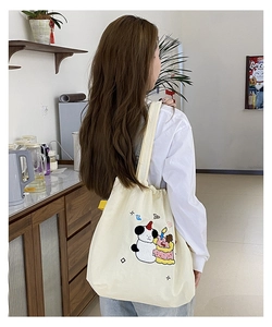 Detailed close-up of a cream canvas tote bag with colorful panda and cake embroidery