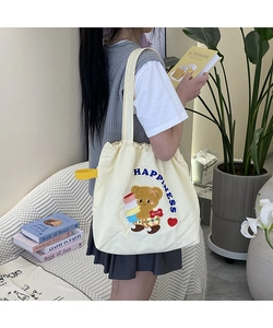 Detail of embroidered brown bear and blue 'HAPPINESS' text on cream canvas tote bag