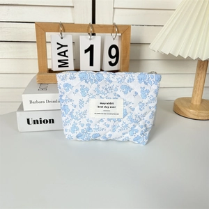 Detailed close-up of blue floral quilted makeup bag with signature woven label