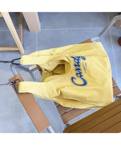 Detail of yellow checkered nylon tote bag with Candy print and metal clasp on wooden chair