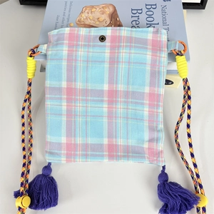 Detail of plaid fabric crossbody bag featuring metal snap button and purple tassels