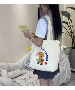 Detail of cartoon bear embroidery and blue Happiness lettering on canvas tote bag