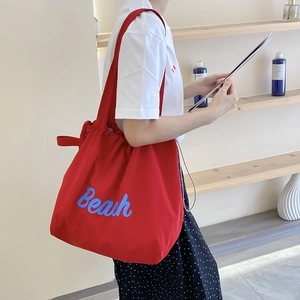 Detail of red nylon tote bag with blue Beach text print worn on model shoulder