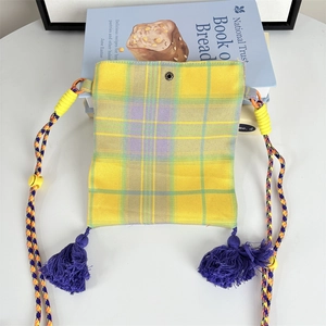 Detail of colorful plaid crossbody bag with purple tassels and adjustable woven strap