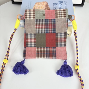 Detailed close-up of patchwork crossbody bag featuring plaid patterns and blue tassels