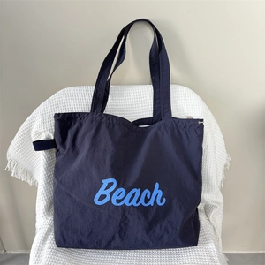 Detail of navy nylon tote bag showing Beach lettering print and drawstring closure
