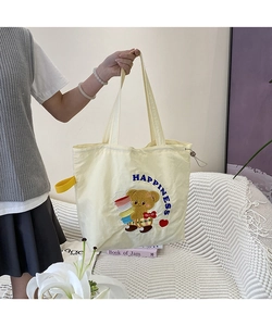 Detail of canvas tote bag showing cute cartoon bear embroidery and yellow strap handle