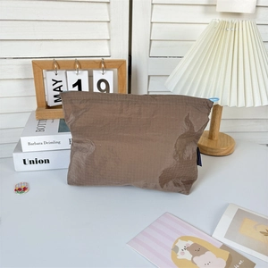 Detailed view of a brown plaid nylon makeup bag with a blue zipper in a cozy setting