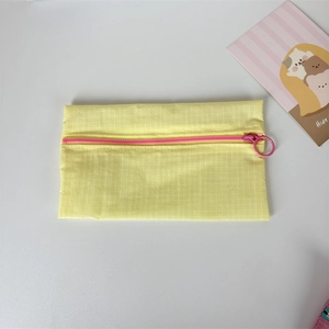 Detail of yellow checkered nylon pouch featuring a contrast pink zipper with large ring puller