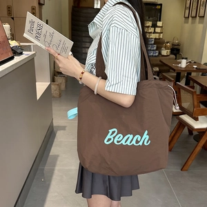 Close-up of brown nylon tote bag with blue Beach lettering and drawstring closure
