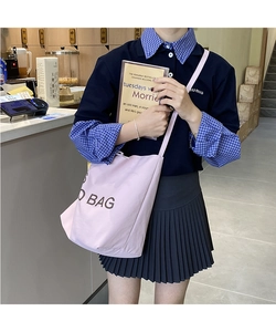 Detail view of pink large capacity tote bag with BAG letter print on shoulder of model