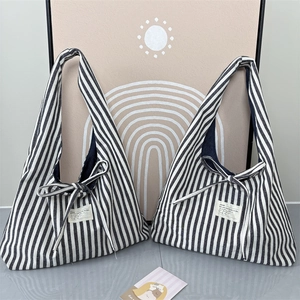 Detail of striped canvas tote bag featuring decorative bow tie and woven label accent