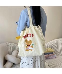 Detail of beige canvas tote bag featuring cute bear embroidery and yellow handle straps
