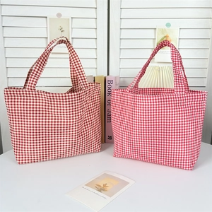 Detailed view of two red gingham canvas tote bags on a rustic white wooden background