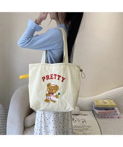 Close-up of embroidered bear and red PRETTY text on a white canvas tote bag