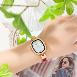 Close-up of gold oval quartz watch with rhinestone bezel and slim red leather strap