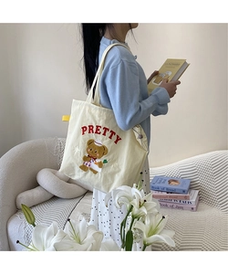 Detail of cute bear embroidery and red PRETTY lettering on cream canvas tote bag