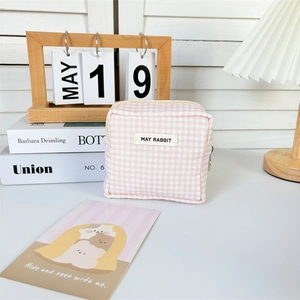 Detail of pink plaid mini cosmetic bag with zipper and May Rabbit label on a white table