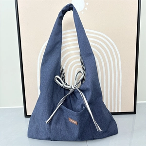 Detail of navy denim tote bag featuring side striped ribbon bow and leather logo patch