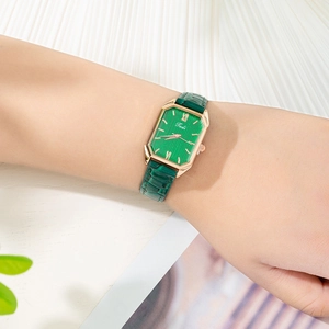 Detalle de un reloj cuadrado verde con caja de oro rosa y correa de cuero esmeralda en la muñeca