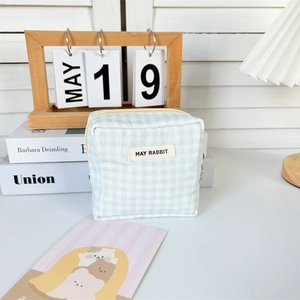 Detail of blue gingham cotton pouch with May Rabbit label on a desk with decor