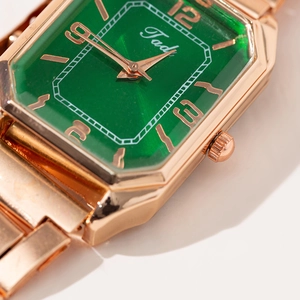 Close-up of octagon rose gold watch with emerald sunray dial and steel strap