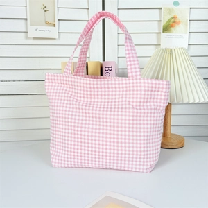 Detail of pink plaid canvas tote bag with dual handles in a warm minimalist setting