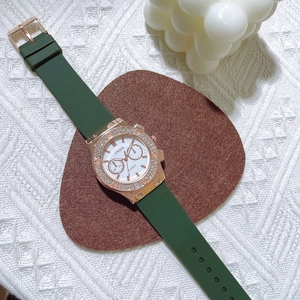 Détail d'une montre en or rose avec bracelet en silicone vert et lunette diamantée