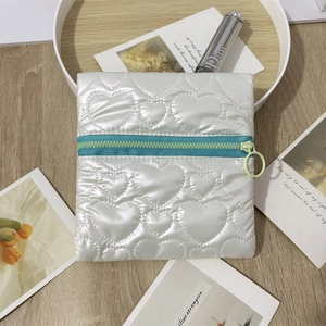 Detail of white heart-shaped quilted PU leather pouch with contrasting green zipper and ring