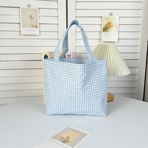 Detail of blue and white checkered canvas tote bag on a white table in minimalist setting