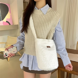 Détail d'un sac seau en peluche blanche avec écusson en cuir marron et bandoulière souple