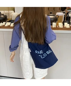 Detail of navy blue nylon tote bag with Paris slogan worn over blue checkered shirt