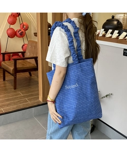 Dettaglio della borsa tote in tela a quadretti blu con ampia tracolla arricciata alla moda