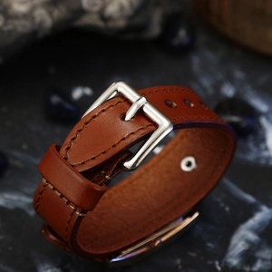 Detail of brown leather watch strap with fine stitching and polished silver pin buckle